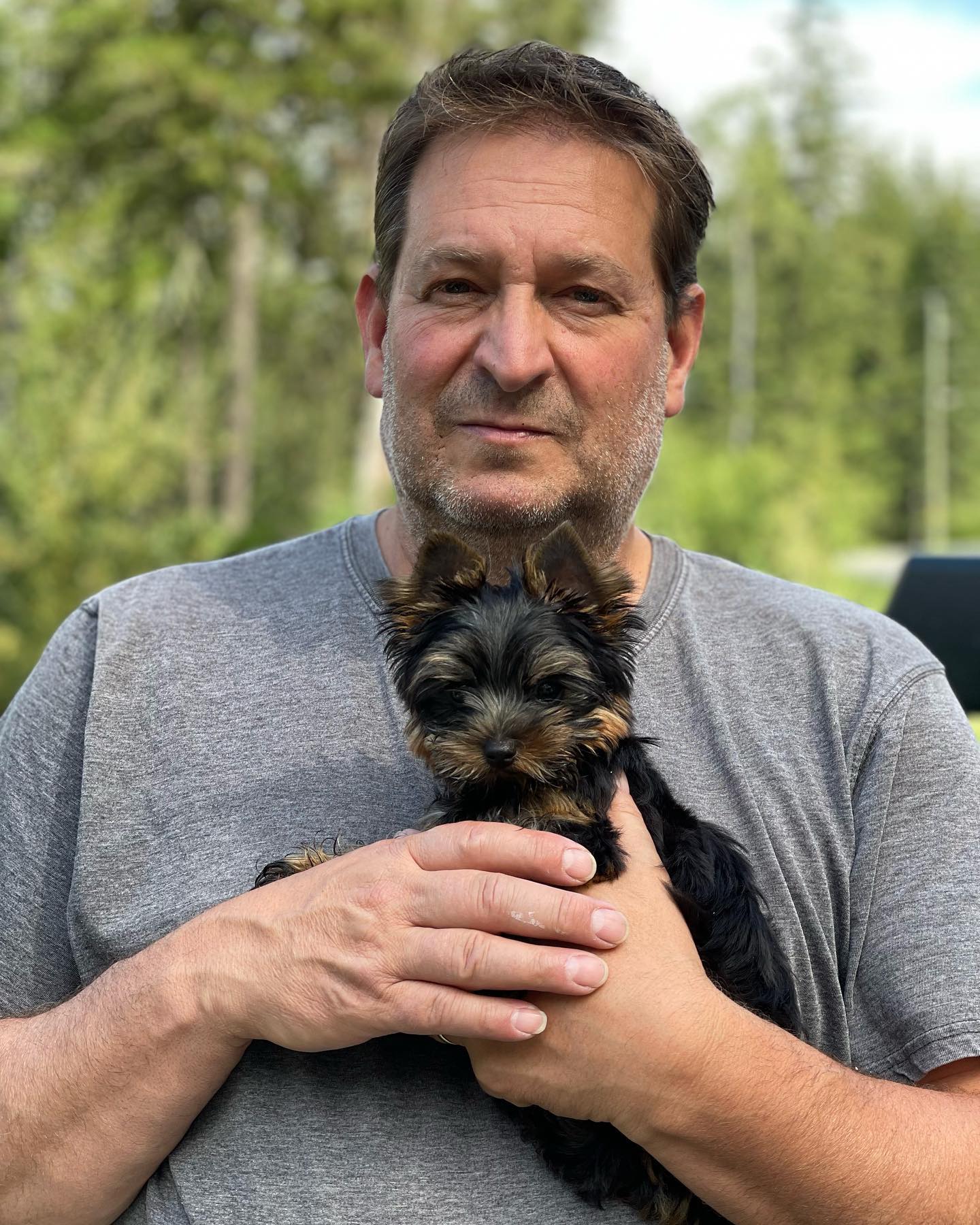 A man holding a small black-and-tan Yorkshire Terrier outdoors.